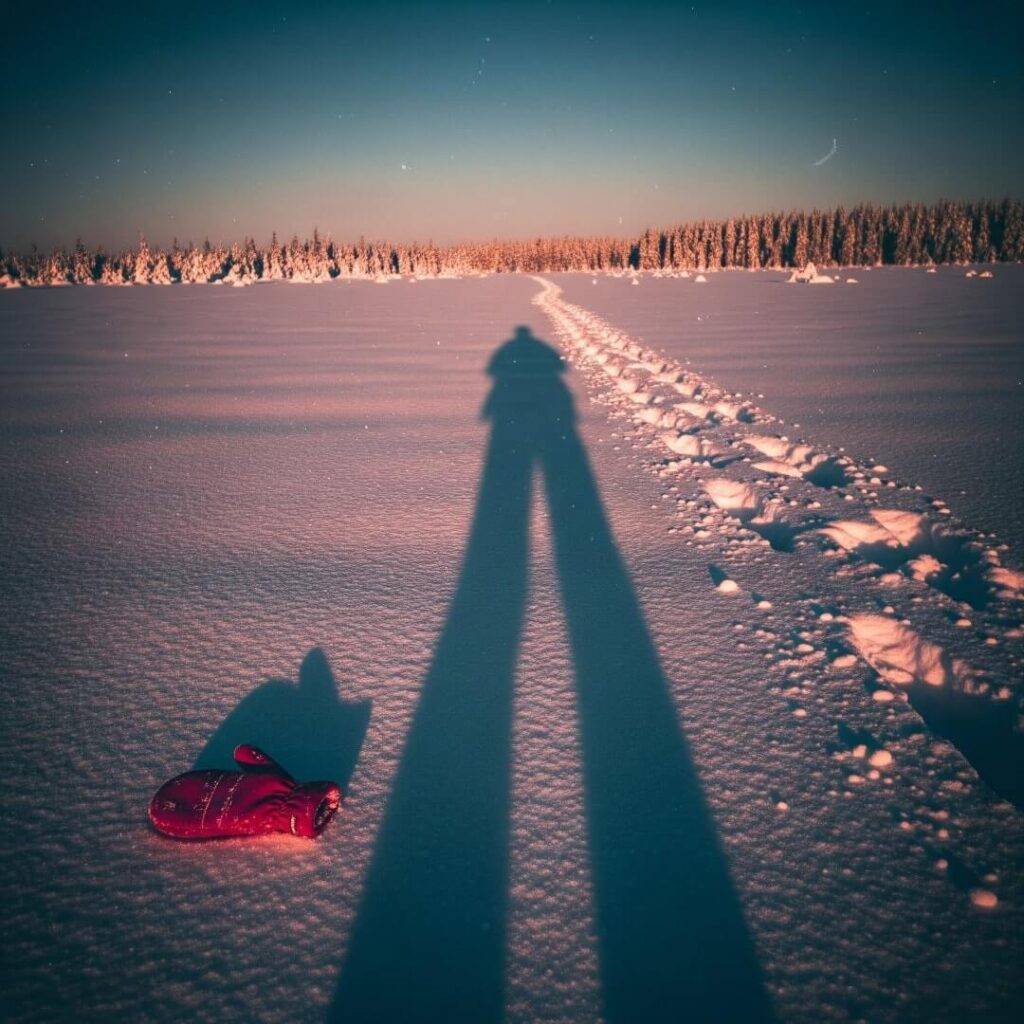 Vintage snowy trail at dusk, long shadow, lost red mitten.